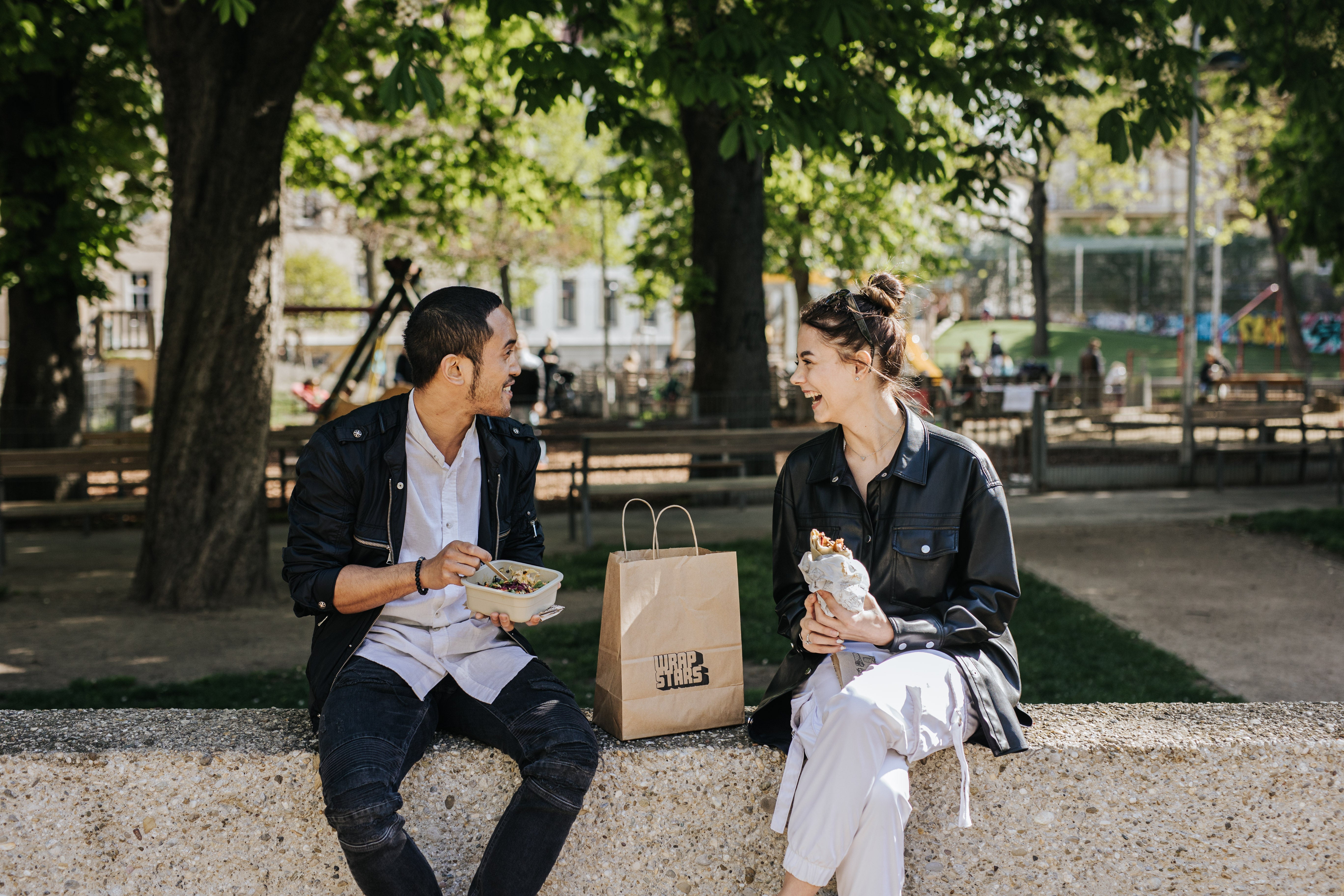 Ein junger Mann und eine junge Frau genießen gemeinsam ein Lunchpakete mit Wraps von Wrapstars Catering