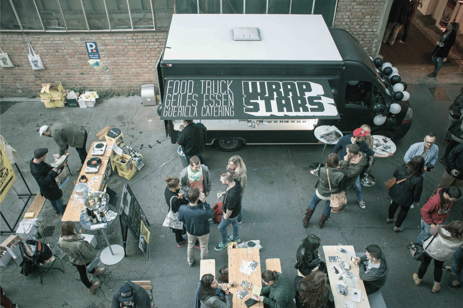 Vogelperspektive von einem Catering mit dem Wrapstars Food Truck in einer entspannten Atmosphäre mit Bierbänken und Drinks.