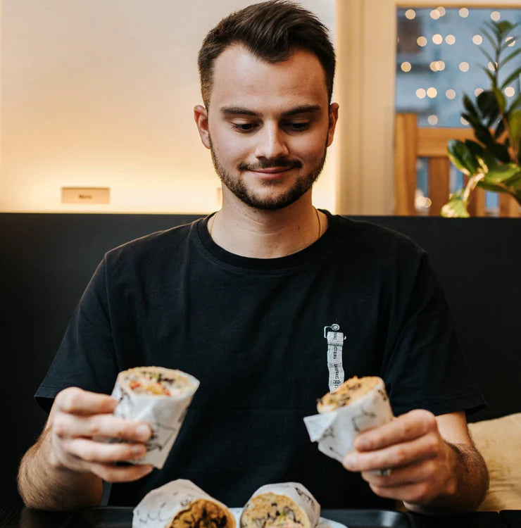 Eine Person gönnt sich gleichzeitig zwei Wraps – mit einem Lächeln im Gesicht.