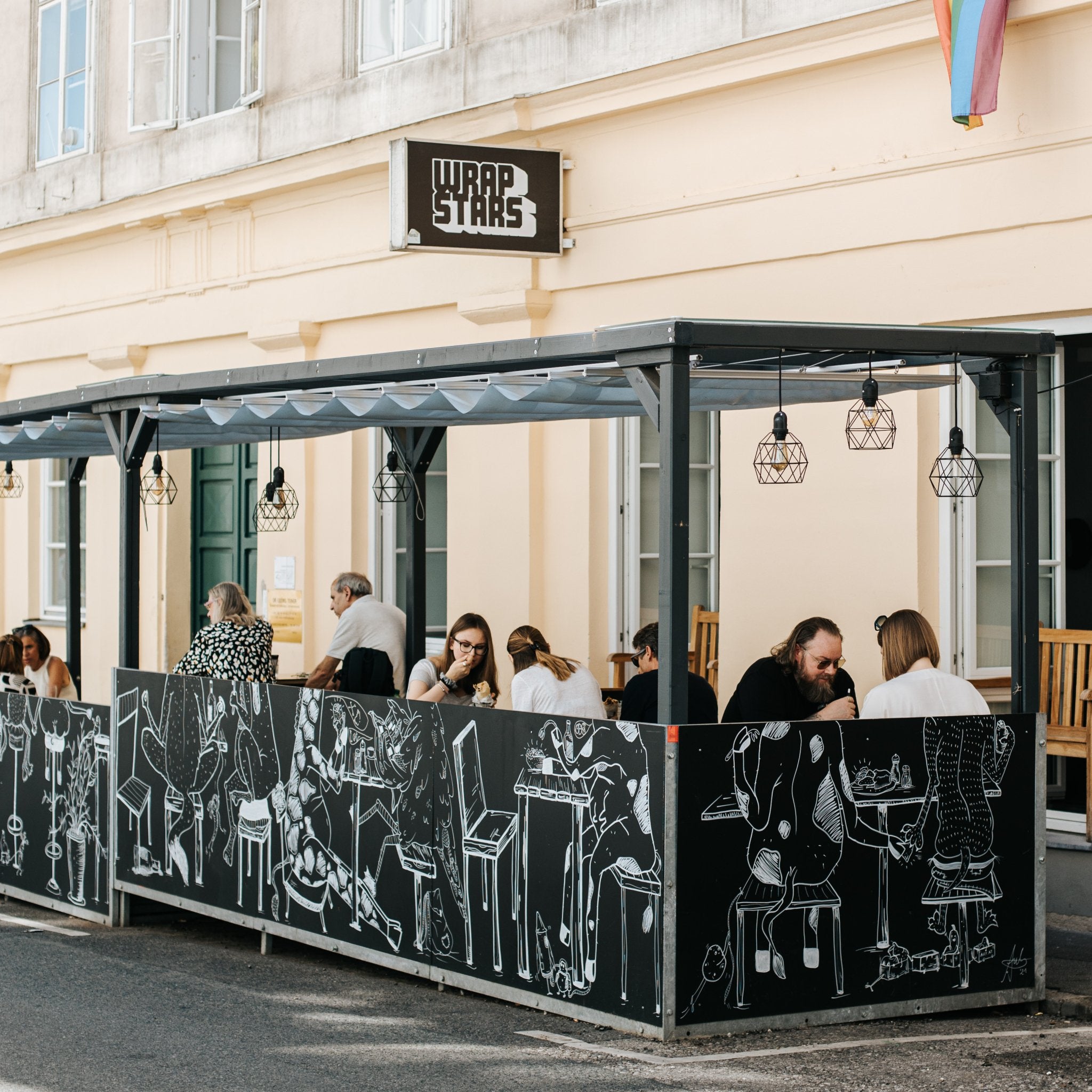 Gastgarten von Wrapstars mit Wandgraffiti und Gästen, die ihre Wraps und Getränke genießen.