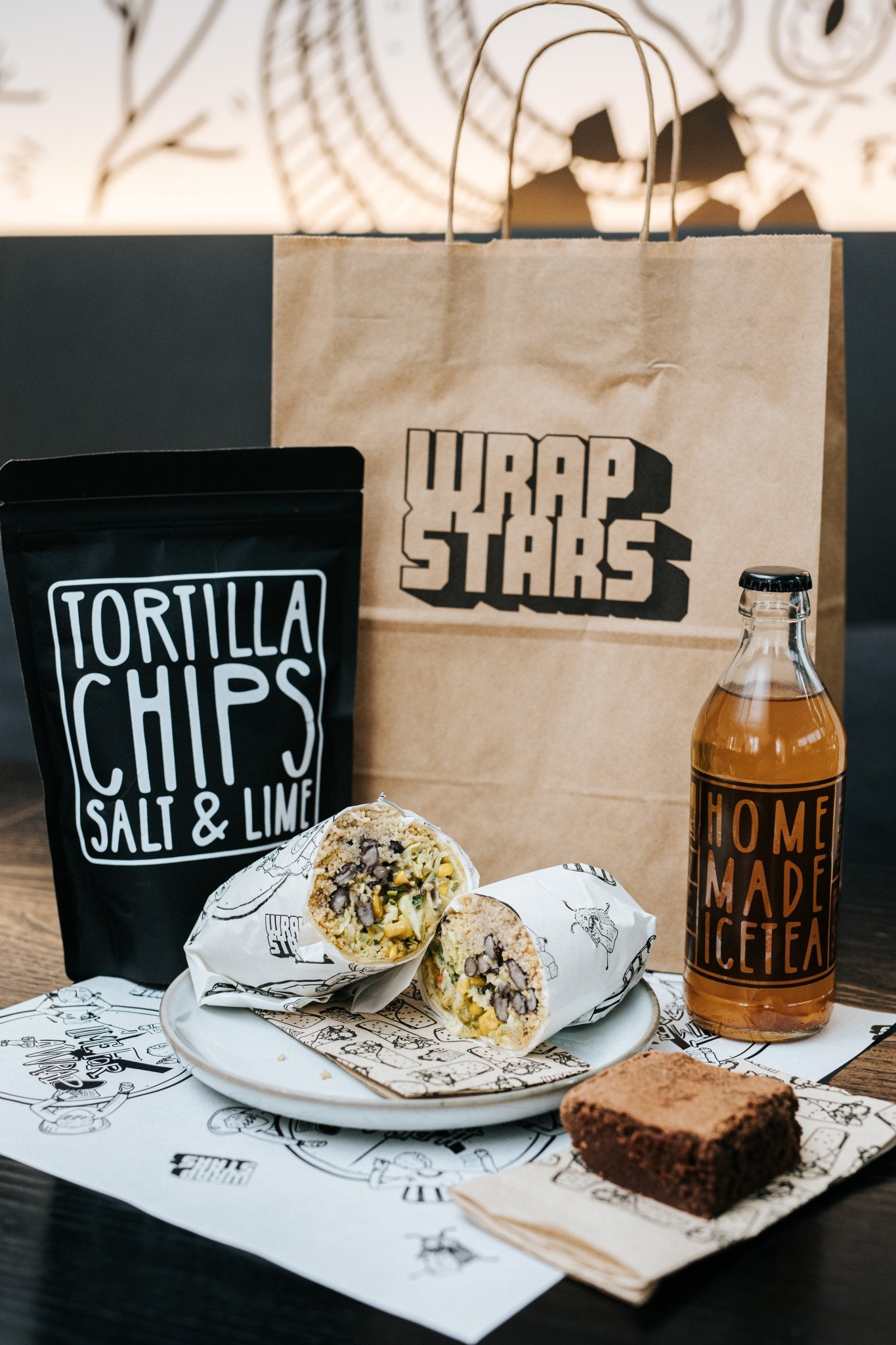 Lunchpaket von Wrapstars mit hausgemachten Tortilla Chips, Haus Eistee und einem aufgeschnittenen Burrito, sowie einem Brownie