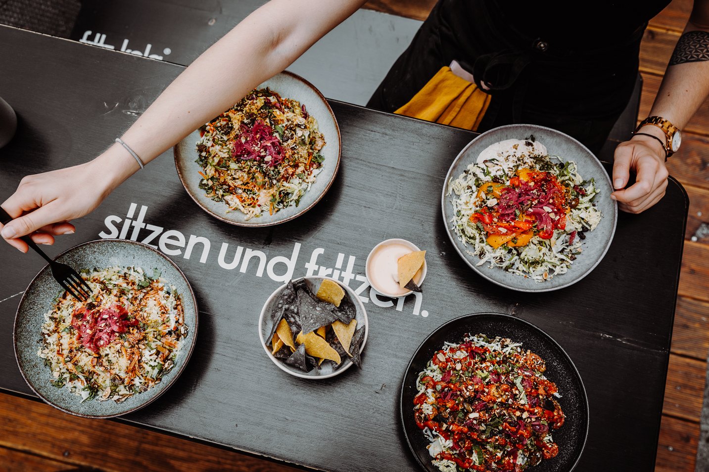 2 Menschen genießen eine Burrito Bowl mit Reis, Salsa und einer Sauce und pickled Veggies und Toppings, sowie Tortilla Chips mit Dip